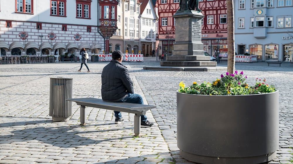 Eine Person sitzt auf dem Marktplatz in Coburg auf einer Bank in der Sonne. / Foto: Daniel Vogl/dpa