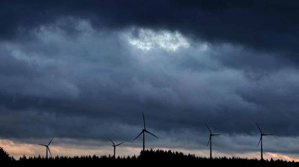 Windräder stehen bei Aitrang im Allgäu unter dichten Regenwolken hinter einem Wald. / Foto: Karl-Josef Hildenbrand/dpa