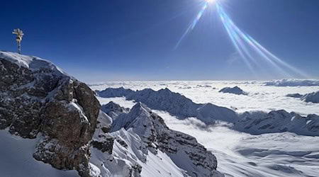 Die Sonne scheint über dem Gipfelkreuz der schneebedeckten Zugspitze. / Foto: Christoph Trost/dpa