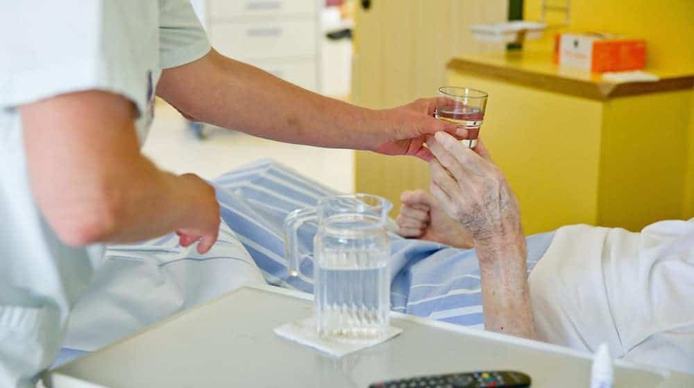 Eine Krankenpflegerin reicht einem Patienten ein Glas Wasser. / Foto: Daniel Karmann/dpa/Archivbild