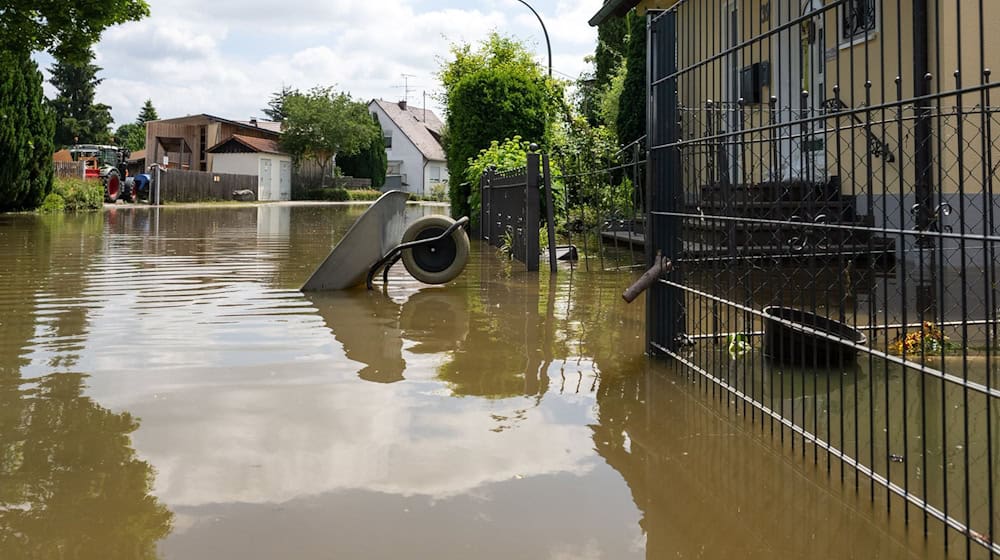 In einer überfluteten Straße ist eine umgekippte Schubkarre vom Wasser umgeben. / Foto: Stefan Puchner/dpa