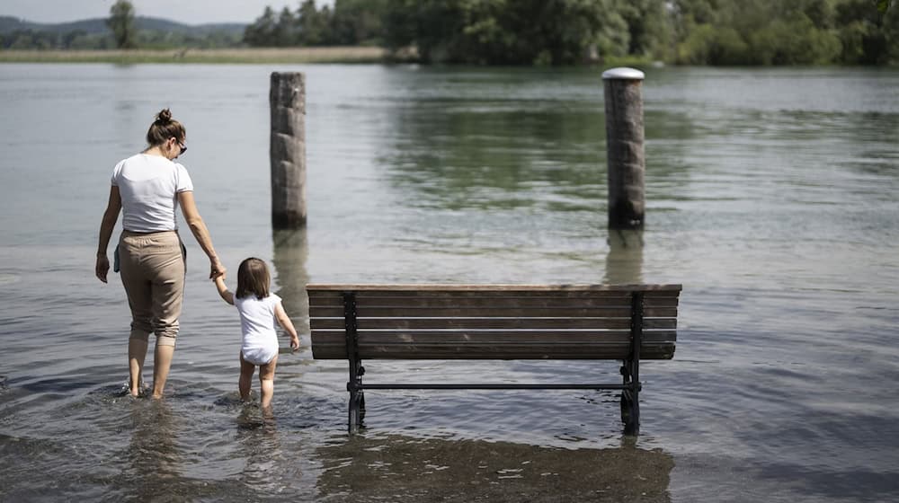 Menschen vergnügen sich am Fluss, der bei Hochwasser über die Ufer getreten ist. / Foto: Gian Ehrenzeller/KEYSTONE/dpa/Symbolbild