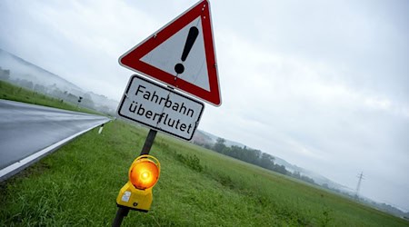 Ein Schild warnt vor Hochwasser, die Straße dahinter ist überflutet. / Foto: Pia Bayer/dpa