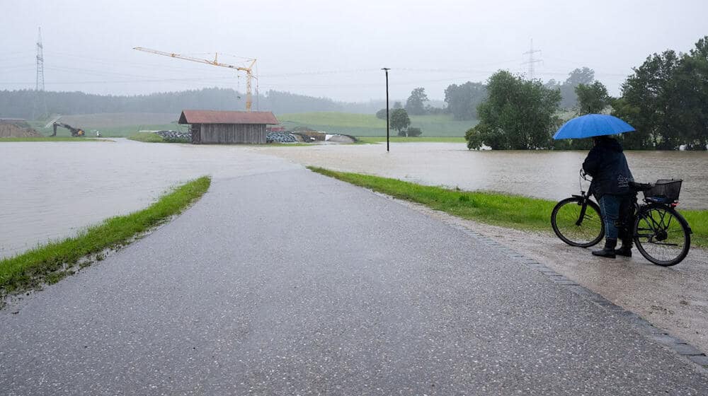 Eine Frau steht mit ihrem Fahrrad an einer überspülten Straße. / Foto: Sven Hoppe/dpa