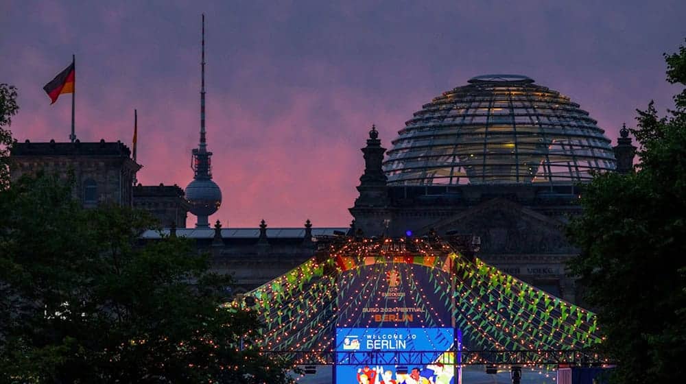 Der Schriftzug «Welcome to Berlin» ist kurz vor Sonnenaufgang auf einem Display der Fanzone (Platz der Republik) vor der Kulisse des Reichstages und des Fernsehturmes zu lesen. / Foto: Soeren Stache/dpa