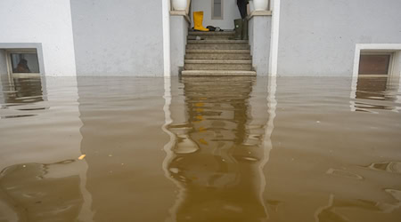 Im Treppenaufgang eines Hauses, dessen Untergeschoss voll Wasser ist, stehen Gummistiefel. / Foto: Stefan Puchner/dpa