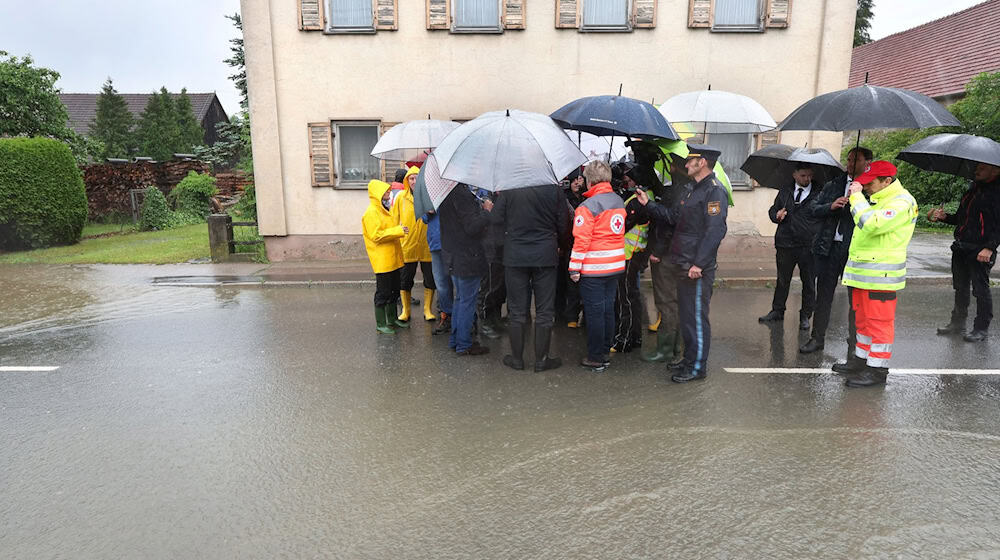Markus Söder (verdeckt) steht, umringt von Journalisten, am Rande einer überfluteten Straße. / Foto: Karl-Josef Hildenbrand/dpa