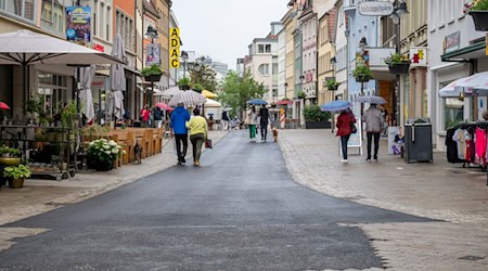 Fußgänger laufen mit Regenschirmen über die Rückertstraße. Der zu dunkle Asphalt der Straße soll nun aufgehellt werden. / Foto: Daniel Vogl/dpa