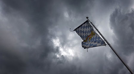 Eine Bayernfahne weht vor dichten Regenwolken im Wind. / Foto: Karl-Josef Hildenbrand/dpa