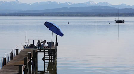 Menschen genießen unter einem Sonnenschirm auf einem Steg die sommerlichen Temperaturen am Ammersee. / Foto: Karl-Josef Hildenbrand/dpa