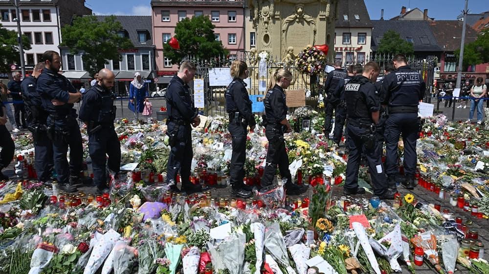 Polizisten stehen auf dem Marktplatz vor einem Gedenkplatz für einen bei einer Messerattacke getöteten Polizisten. / Foto: Bernd Weißbrod/dpa
