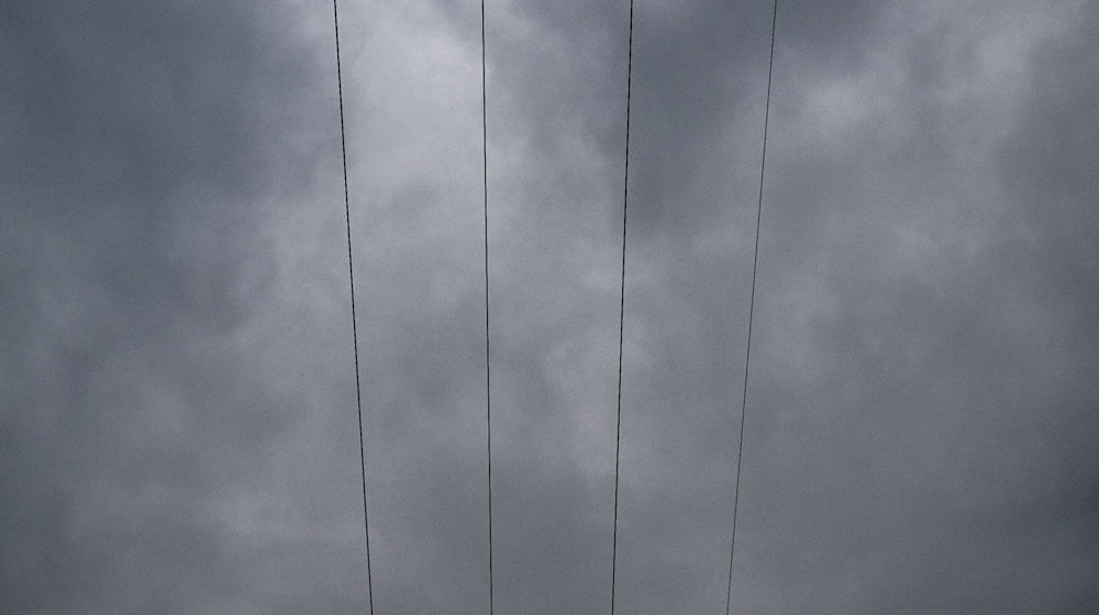 Über den Leitungen eines Strommastes durchziehen Wolken den Himmel. / Foto: Pia Bayer/dpa