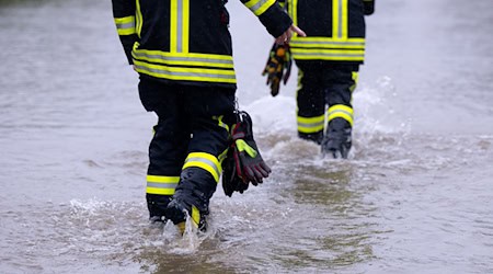 Feuerwehrleute gehen über eine überflutet Straße. / Foto: Sven Hoppe/dpa