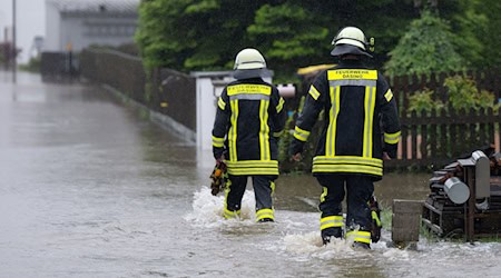 Feuerwehrleute gehen über eine überflutet Straße in Dasing. / Foto: Sven Hoppe/dpa