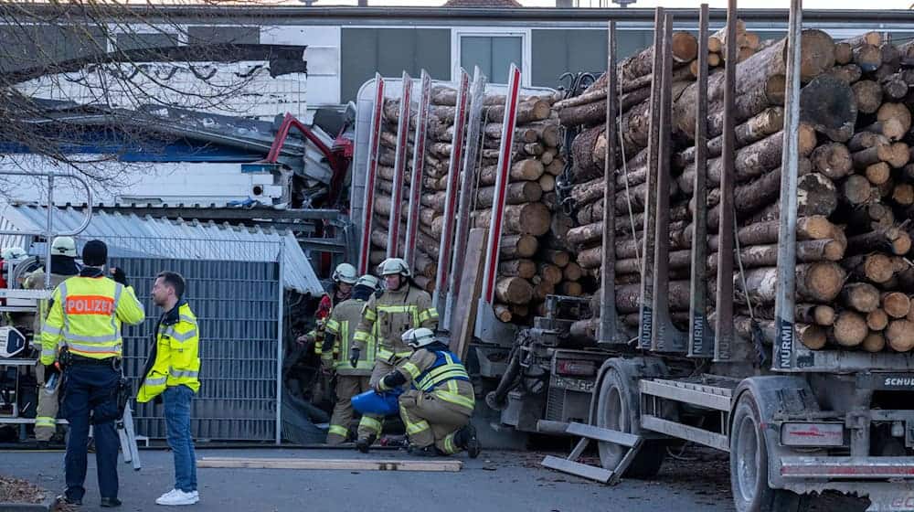 Ein Holzlaster steckt mit dem Führerhaus in einem Gebäude. Die Polizei geht davon aus, dass der Fahrer wegen eines medizinischen Notfalls die Kontrolle über den Laster verlor. / Foto: Pia Bayer/dpa