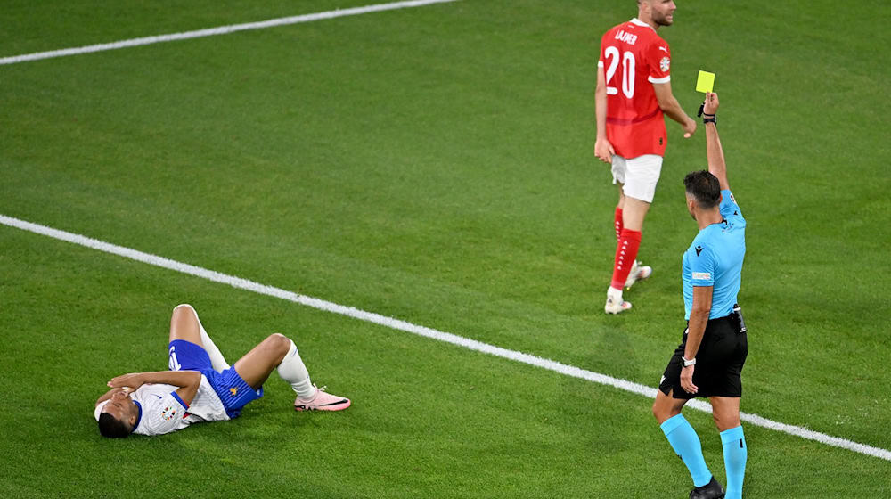 Schiedsrichter Jesús Gil Manzano zeigt dem Österreicher Konrad Laimer (m) Gelb nach einem Foul an Kylian Mbappé. / Foto: Fabian Strauch/dpa