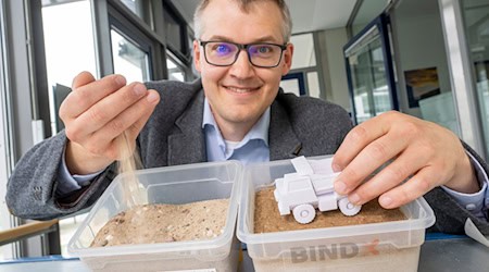 Luitpold Fried vom Start-Up-Unternehmen „Bind-X“ zeigt an einem Beispiel, wie mit einem speziellen Bindemittel aus ungefestigtem Sand, eine feste Verbindung entstehen kann, die zur Reduzierung von Staub auf unbefestigten Straßen führt.  / Foto: Peter Kneffel/dpa