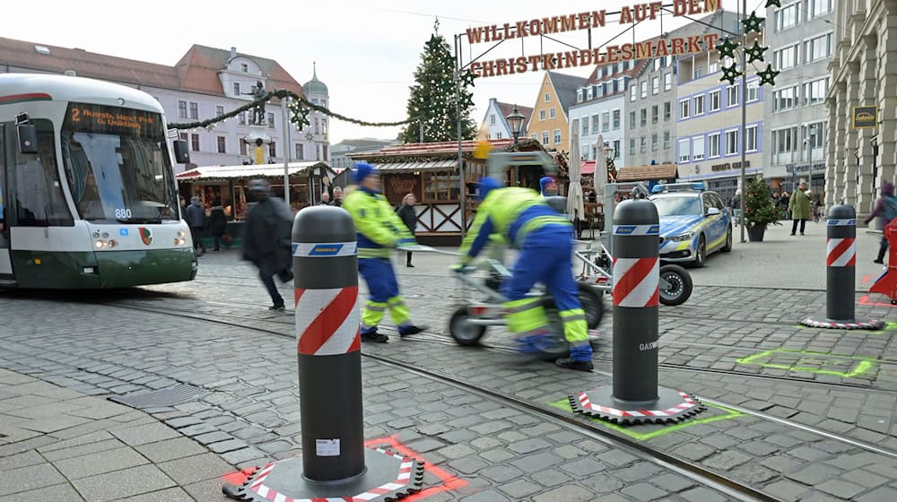 Zu den Hauptverkehrszeiten müssen Sicherheitsmitarbeiter neben dem Augsburger Christkindlesmarkt jede Stunde dutzendfach schwere Poller bewegen, damit die Straßenbahnen durchfahren können. / Foto: Malin Wunderlich/dpa