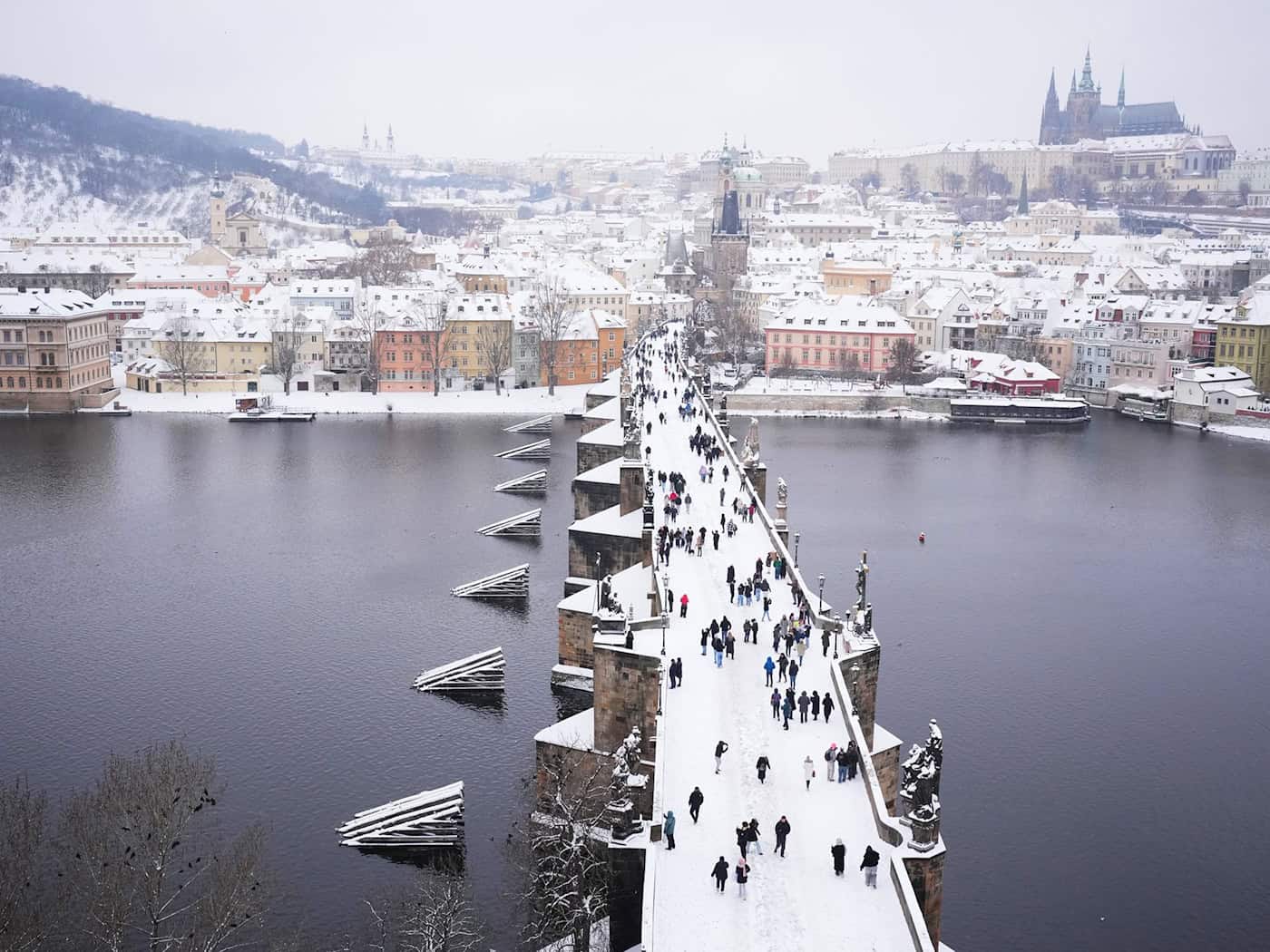 Menschen überqueren die mittelalterliche Karlsbrücke nach starkem Schneefall. / Foto: Petr David Josek/AP/dpa