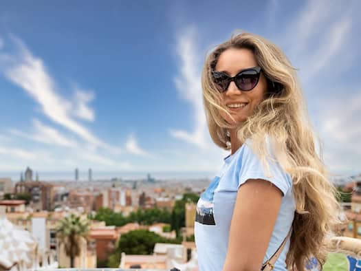 Eine lächelnde Frau mit Sonnenbrille genießt den Ausblick über Barcelona vom Park Güell aus.