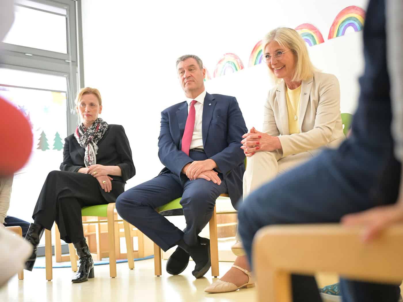Bunte Regenbögen an der Wand und ein Stuhlkreis: In dieser Umgebung stellen sich Karin Prien, Markus Söder und Ulrike Scharf den Fragen von Vorschulkindern. / Foto: Malin Wunderlich/dpa