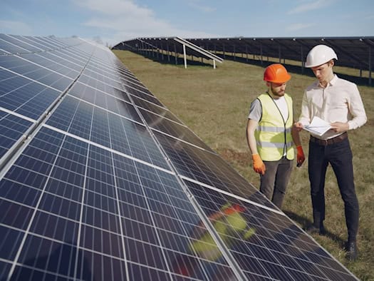 Zwei Fachleute besprechen Pläne auf einem großen Solarpark in Bayern mit Photovoltaik-Modulen auf einer Freifläche.