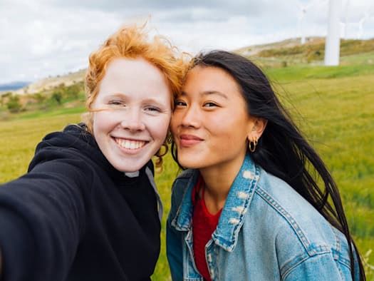 Zwei lächelnde Frauen machen ein Selfie in einer grünen Landschaft.