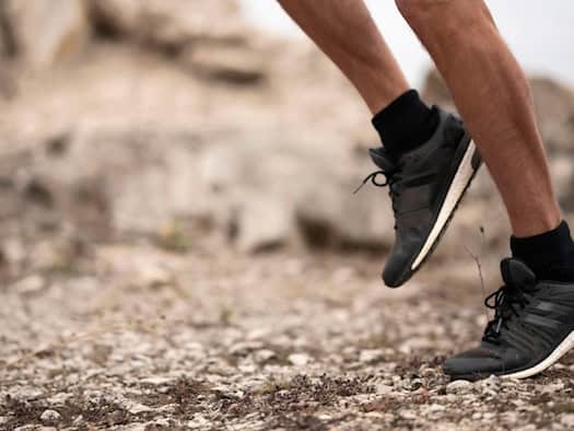 Läuferfüße mit schwarzem Laufschuh auf steinigem Boden – Symbol für die Bedeutung der Sprengung.