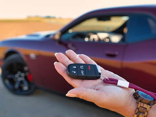 Hand hält Autoschlüssel vor einem roten Auto – Symbol für digitale Fahrzeugzulassung und moderne Mobilität.