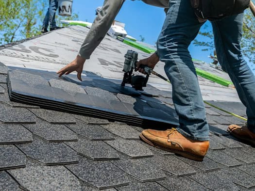 Handwerker arbeitet mit einem Nagler auf einem Dach mit Schindeln.