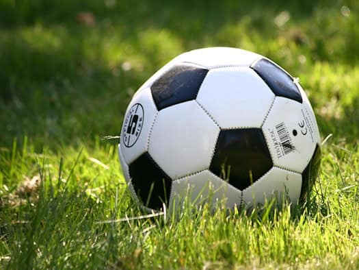 Ein Fußball liegt auf einem grünen Rasenfeld im Sonnenlicht.
