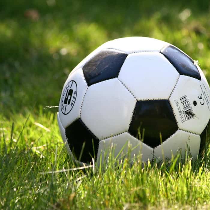 Ein Fußball liegt auf einem grünen Rasenfeld im Sonnenlicht.