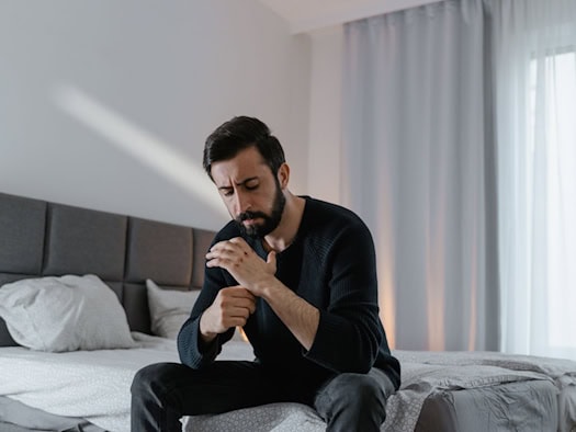 Mann sitzt nachdenklich auf dem Bett