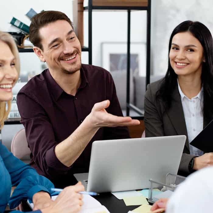 Engagiertes Team bei kreativer Besprechung im Büro, eine Person arbeitet am Laptop, eine andere präsentiert eine Idee
