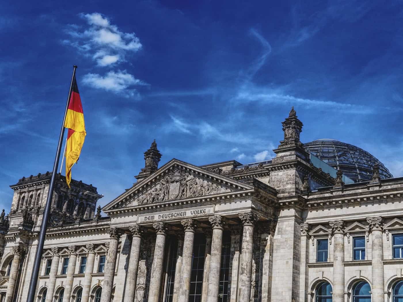 Reichstagsgebäude in Berlin mit deutscher Flagge und blauem Himmel