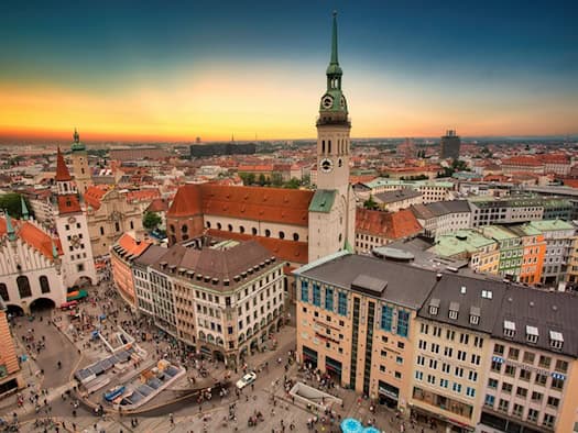 Stadtansicht von München bei Sonnenuntergang mit belebtem Platz, historischen Gebäuden und einem Kirchturm