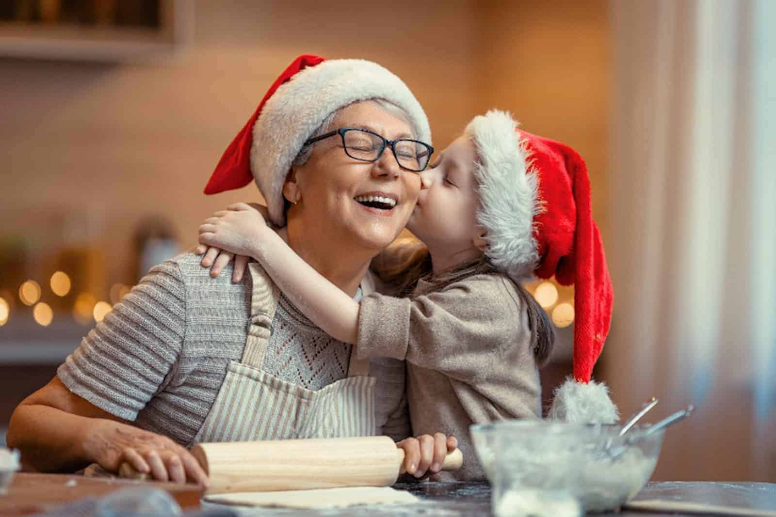 Vor den Festtagen backen Oma und Enkelin gemeinsam Kekse. Das macht viel Freude und Oma bekommt nicht nur eine Umarmung, sondern auch einen Kuss.