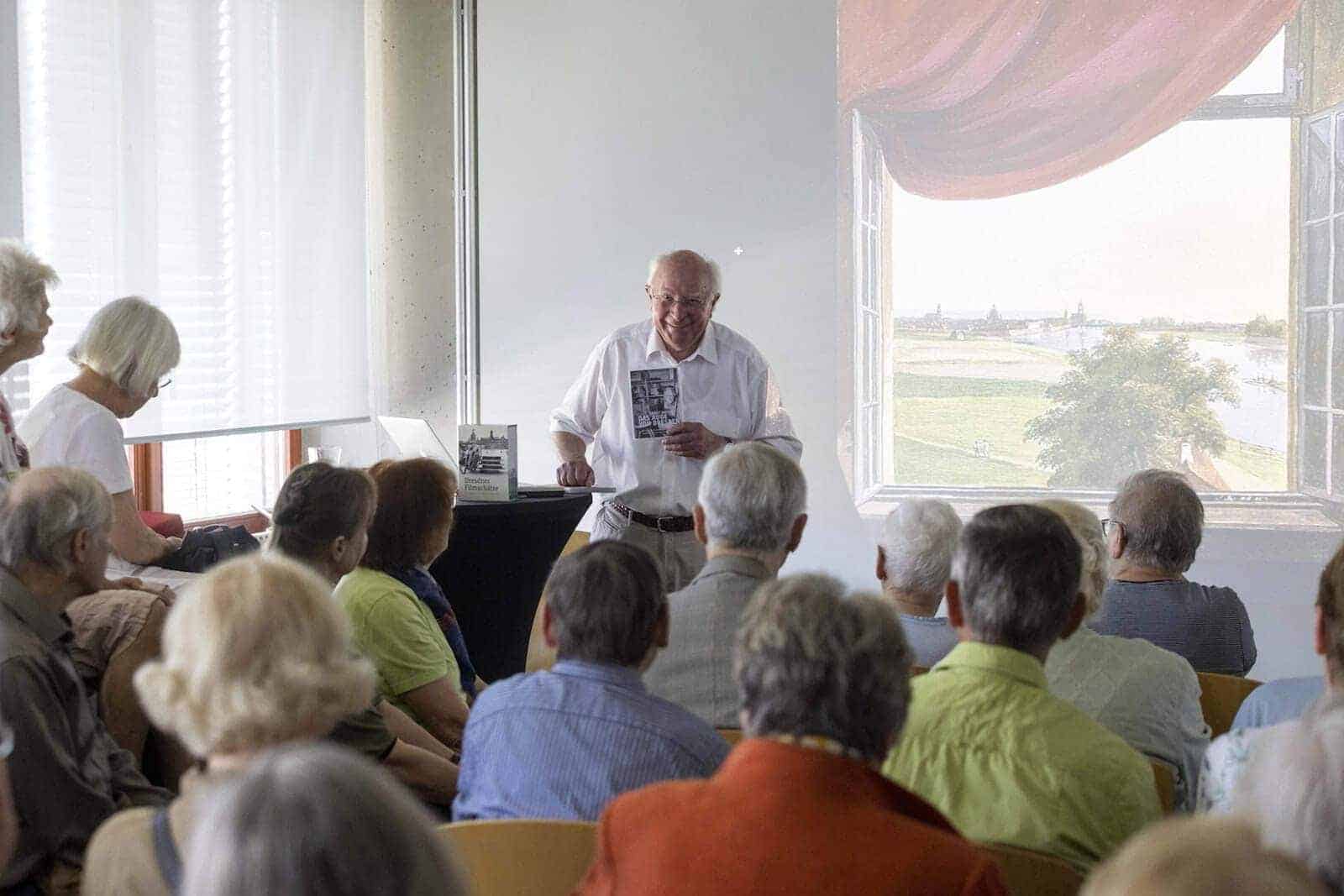 Vor aufmerksamen Zuhörern referiert der bekannte Kameramann Ernst Hirsch. Im Hintergrund: Eine Leinwand, die ein offenes Fenster mit Blick in die Landschaft zeigt.