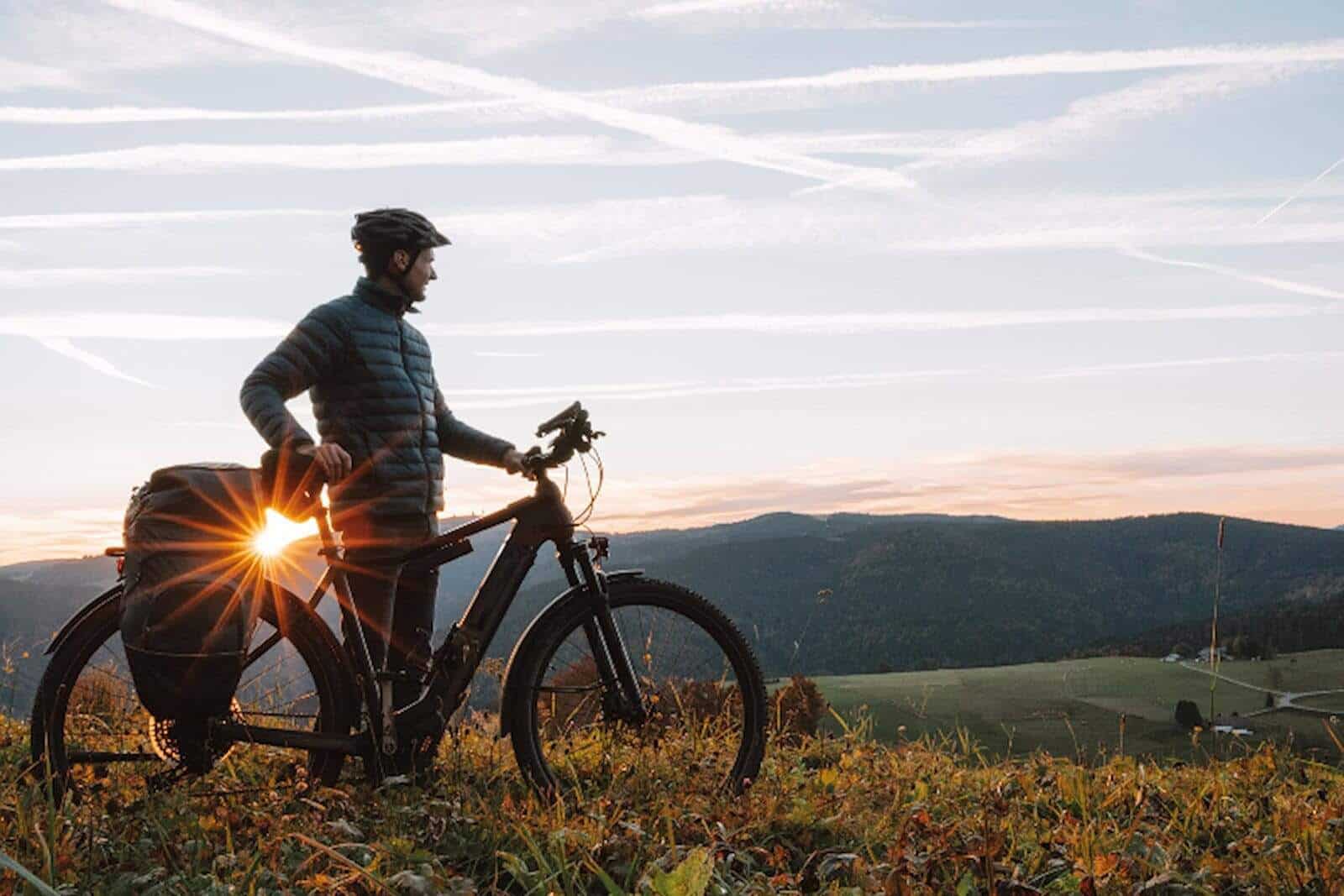 E-Bike Fahrer ist vom Rad abgestiegen und schaut in das Abendlicht in einer Landschaft.
