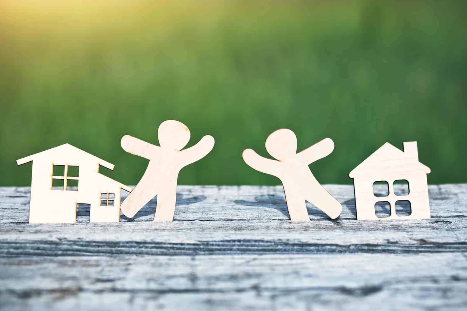 Aus Holz zwei Häuser und zwei Menschen, die in der Mitte stehen und einander zugeneigt sind. Foto: StockAdobe/Ivan Kruk