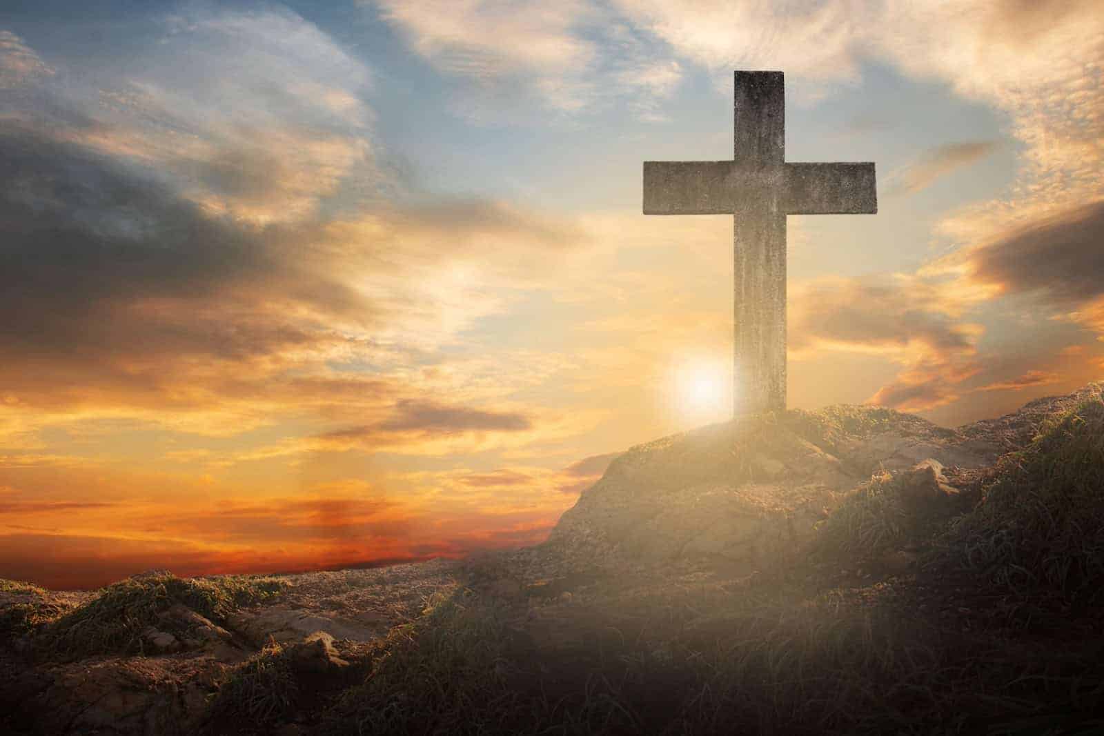 Ein Kreuz steht auf dem Berg und die Sonne geht unter.