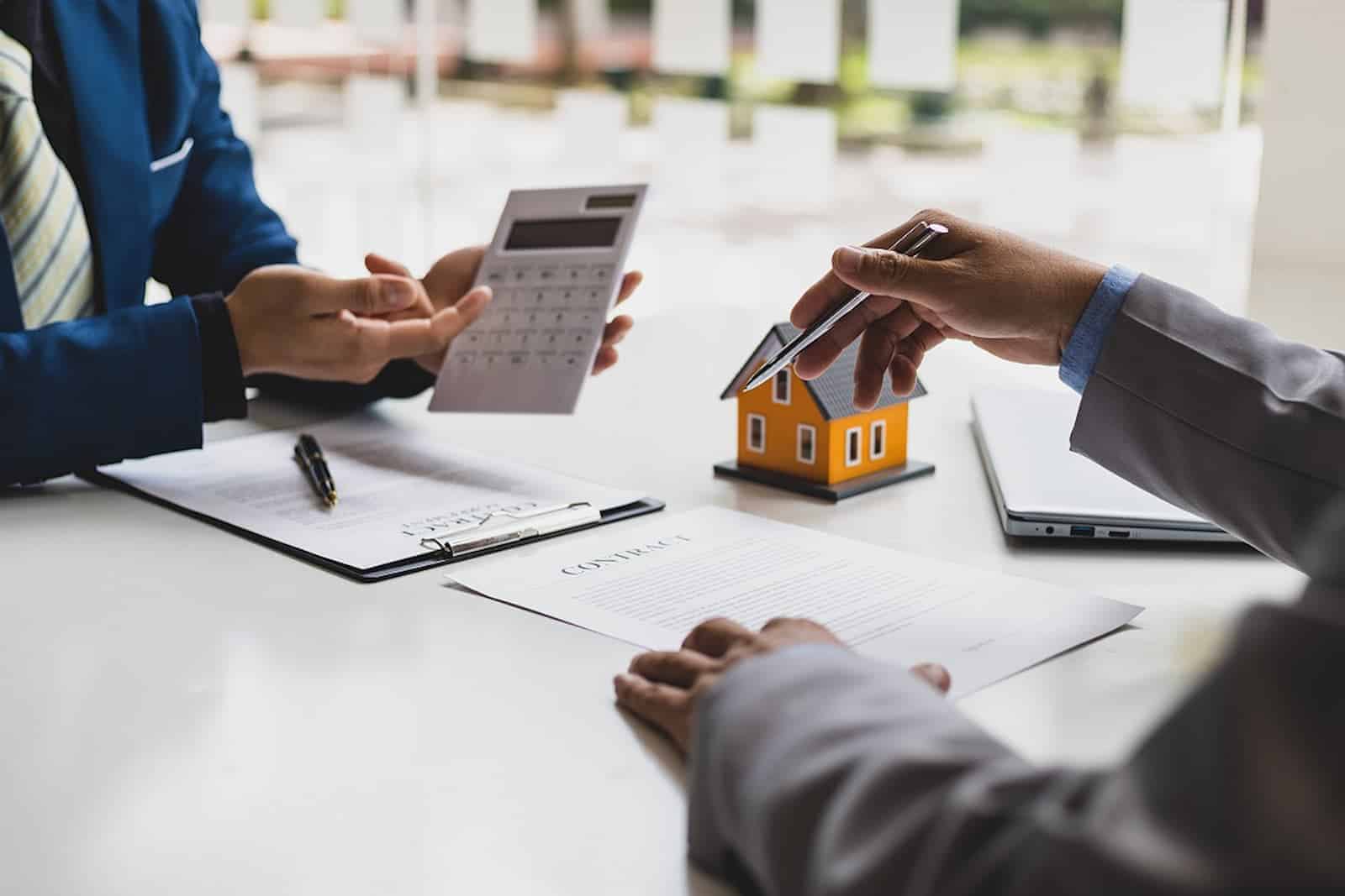 Ein Haus muss neu geschätzt werden. Zwei Menschen sitzen am Tisch und füllen gemeinsam die Unterlagen aus. Für die Kalkulation wird ein Taschenrechner