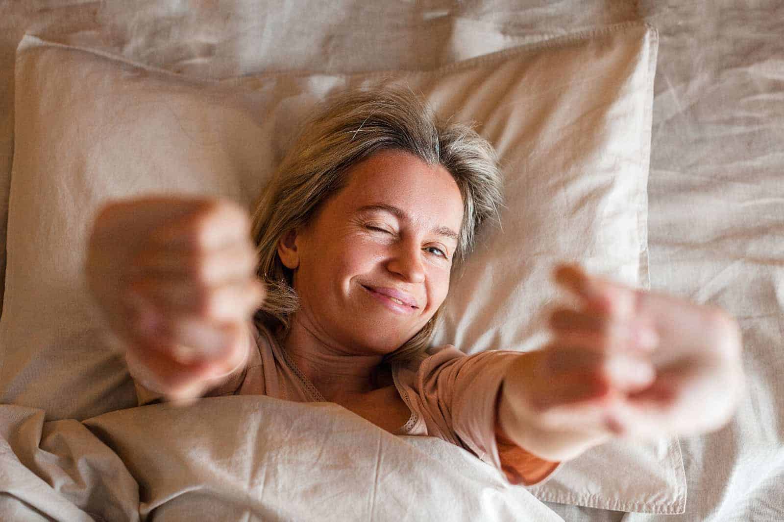 Frau dehnt sich morgens fröhlich im Bett