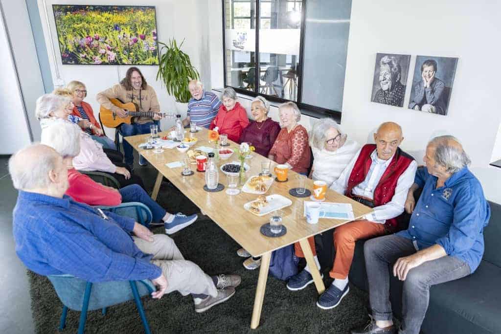 Senioren sitzen mit einem jungen Gitarrenspieler am Kaffeetisch.