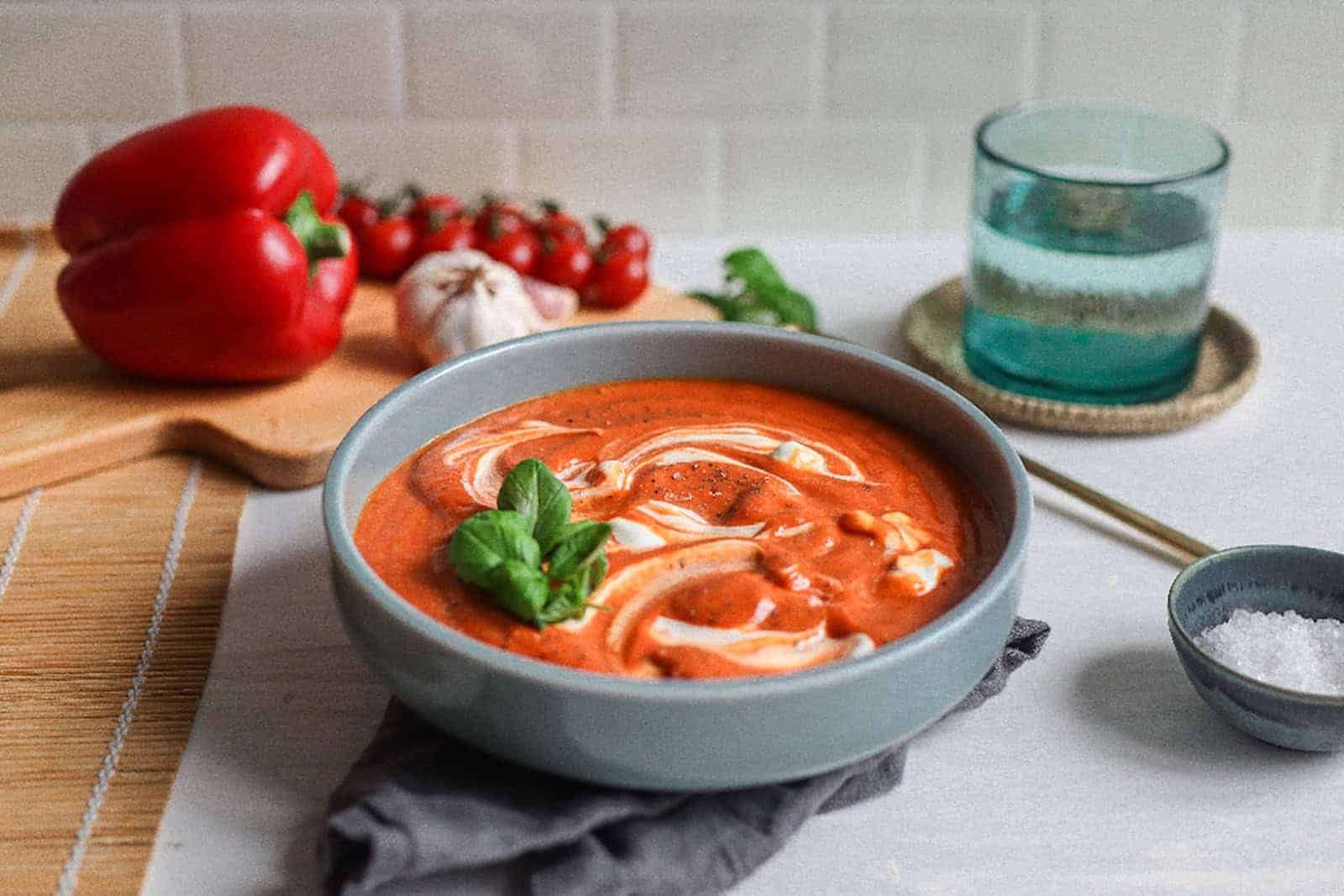 Eine Schale mit roter super steht auf dem Tisch. Daneben liegt Paprika. Ein Glas Wasser steht auf einem Untersetzer.