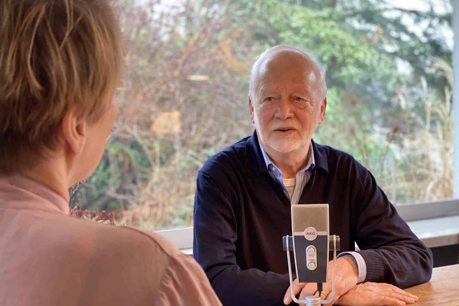 Senior sitzt vor Mikrofon im Gespräch.