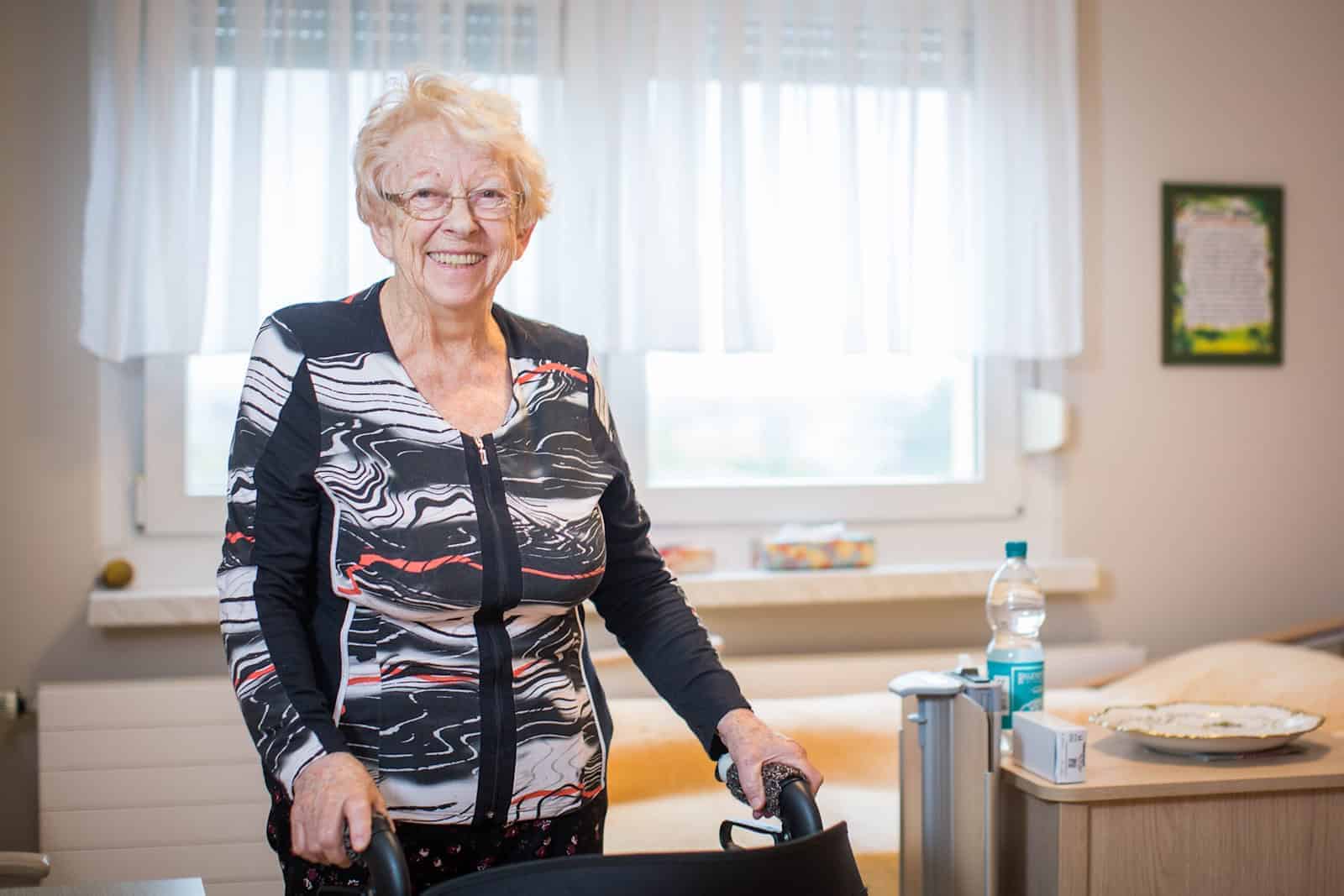 Dame steht im Zimmer mit Rollator.