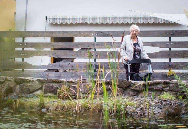 Seniorin Rosemarie John geht mit ihrem Rollator vor dem Seniorenheim spazieren im Park.