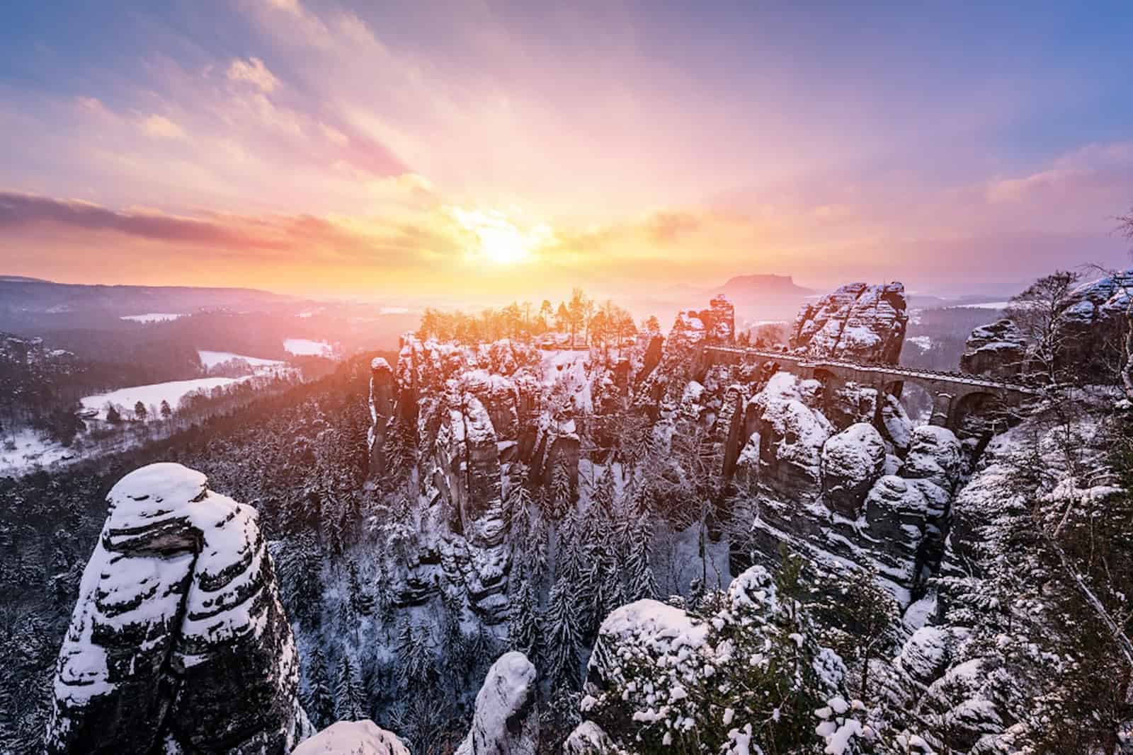 Hinter den zerklüfteten, markanten Felsen der Sächsischen Schweiz geht die Sonne im Abendrot unter.