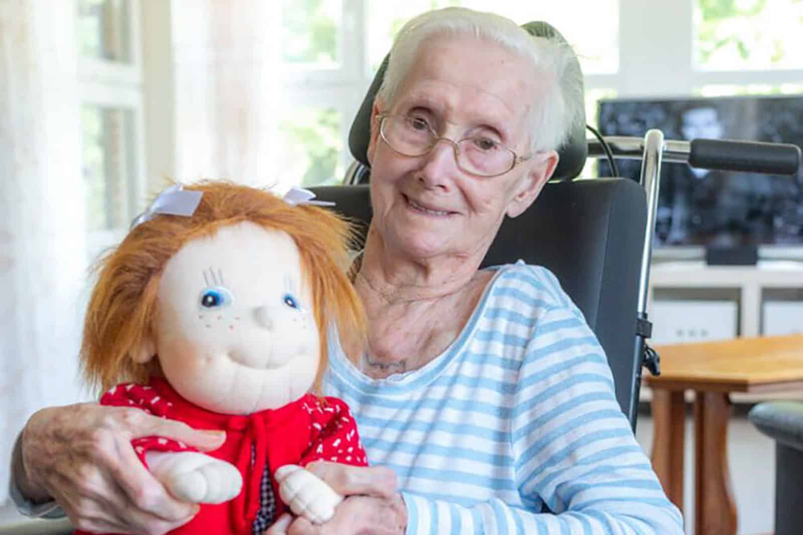 Seniorin im Rollstuhl, Empathie-Puppe im Arm.